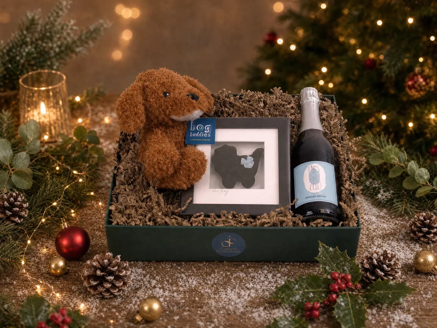 The Hello Baby Boy hamper dressed for Christmas, a soft toy and a photo frame beside a bottle of sparkling wine