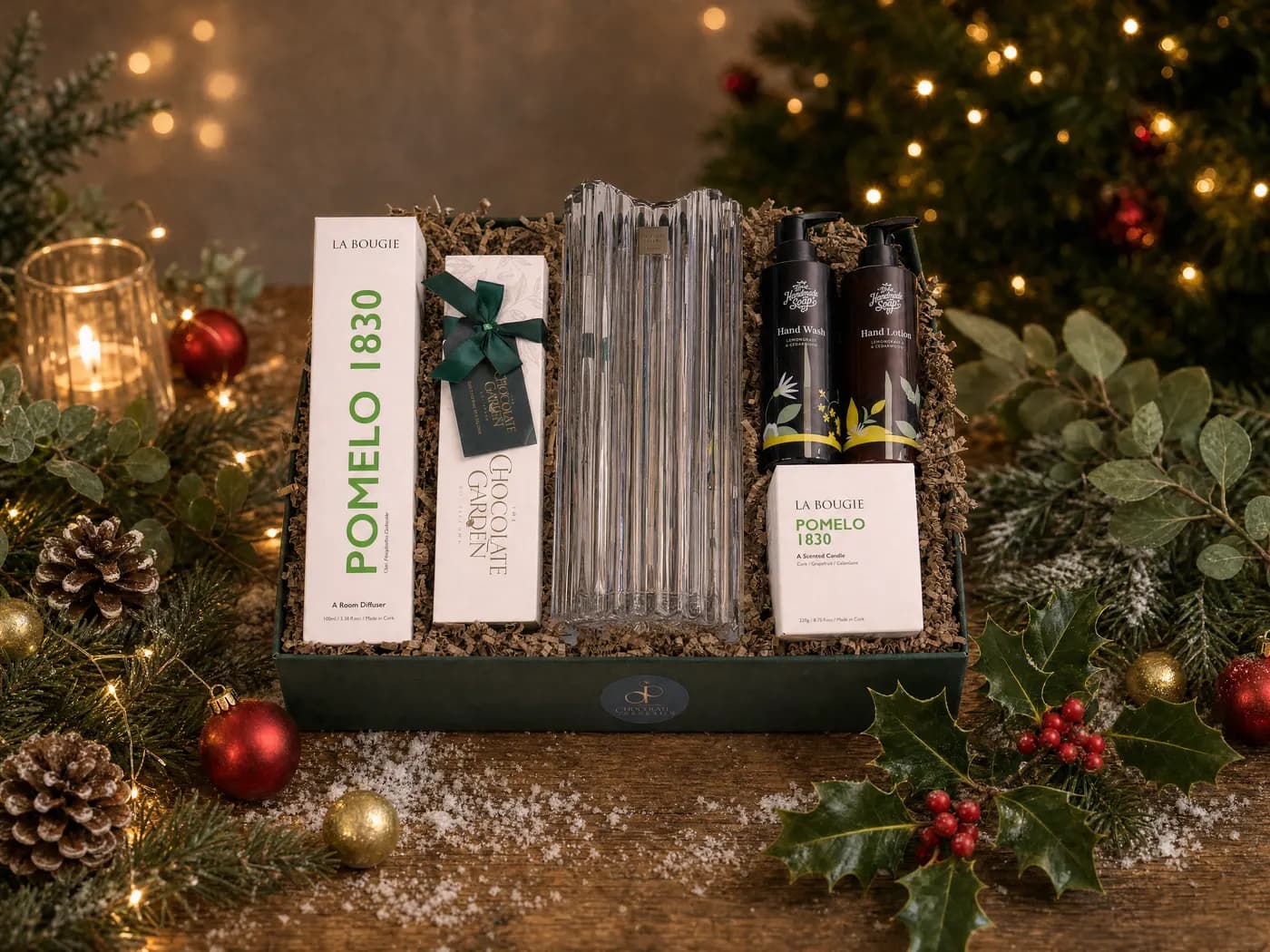 The Luxury Home and Indulgence Hamper dressed for Christmas, a fluted crystal vase flanked by a La Bougie Pomelo candle and diffuser and a box of chocolates