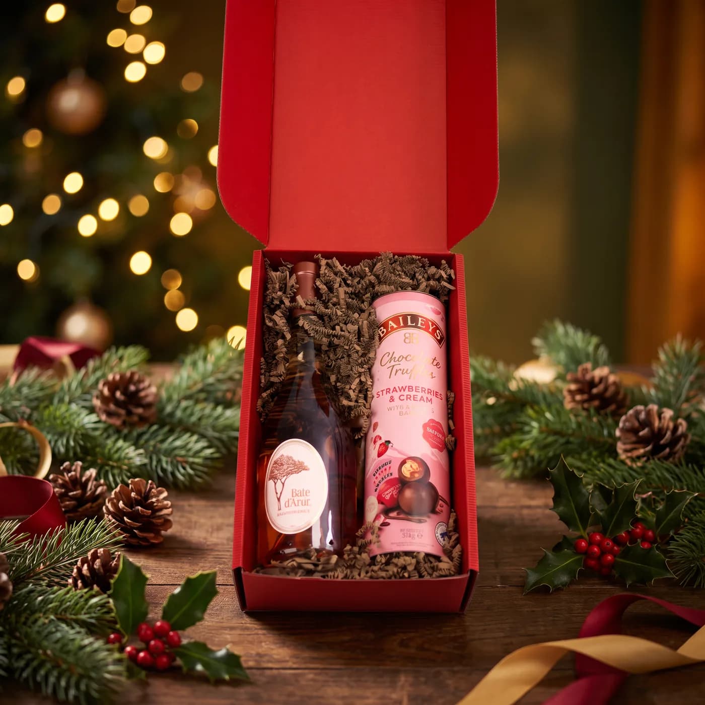 The Perfect Duo dressed for Christmas, a red gift box holding a bottle of Baie d’Azur rosé and a tube of Baileys Strawberries and Cream chocolates, with pine, holly and pinecones around it